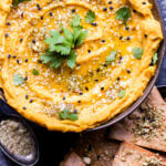 Butternut Squash Hummus in a bowl topped with dukkah and cilantro. Pita chips next to the bowl.