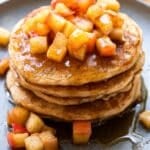 A stack of apple cinnamon pancakes topped with sautéed cinnamon apples.