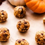 Pumpkin Pie Energy Bites on parchment paper with mini white and orange pumpkins in the background.