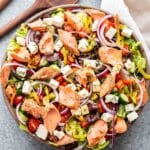 Greek Salmon Salad in a white salad bowl with wooden serving spoons next to it.