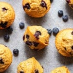 Blueberry muffins on a gray countertop with blueberries scattered around them.