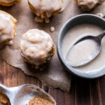 Overhead photo of Mini Chai Muffins with Vanilla Bean Glaze on parchment paper with a teaspoon of chai spice in front of them and a bowl of the glaze next to them.