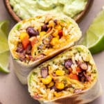 Black Bean and Veggie Burrito cut in half and standing up so you can see inside. A bowl of guacamole is behind it.