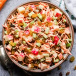 Overhead photo of Carrot Apple Salad with Yogurt Dressing in white bowl with spoons next to bowl and carrots behind it.