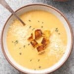 Creamy Cauliflower Soup in a white bowl with a spoon topped with croutons.