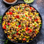 Mexican Quinoa Salad with Honey Lime Vinaigrette in black bowl with a small bowl of vinaigrette and squeezed limes in the background.