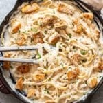 Tongs picking up Chicken Fettuccine Alfredo out of a skillet.