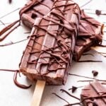Two Greek Yogurt Fudgesicles. One on top of the other with a bite taken out of it and melted chocolate drizzled over them.