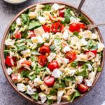 Spinach Orzo Chicken Salad with Goat Cheese, cherry tomatoes and roasted red peppers in a bowl with serving spoons.