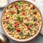 Orzo with Spinach and Roasted Red Peppers in a white serving bowl with a small bowl of parmesan cheese behind it.