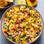 Peach Green Chile Corn Salsa in a white bowl with tortilla chips, half of a peach, and a lime behind it.