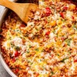 Overhead photo of a metal skillet full of the stuffed pepper casserole. It's made with ground turkey, rice, tomato sauce, red and yellow bell peppers and topped with melted cheese. A wooden serving spoon is in the skillet.