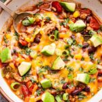 White bowl with Turkey Taco Soup in it. Topped with melted cheese, avocado and green onions.