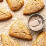 Pumpkin scones on parchment paper with a bowl of cinnamon sugar.