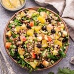 Winter Kale and Wild Rice Salad in a white serving bowl with a small bowl of the vinaigrette behind it and a dish towel.
