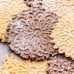 vanilla and chocolate pizzelles scattered on top of each other and dusted with powdered sugar.