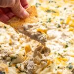 Hand scooping up green chile chicken enchilada dip.