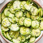 Overhead photo of Asian Cucumber Sesame Salad in a white bowl with a small bowl of sesame seeds behind it.