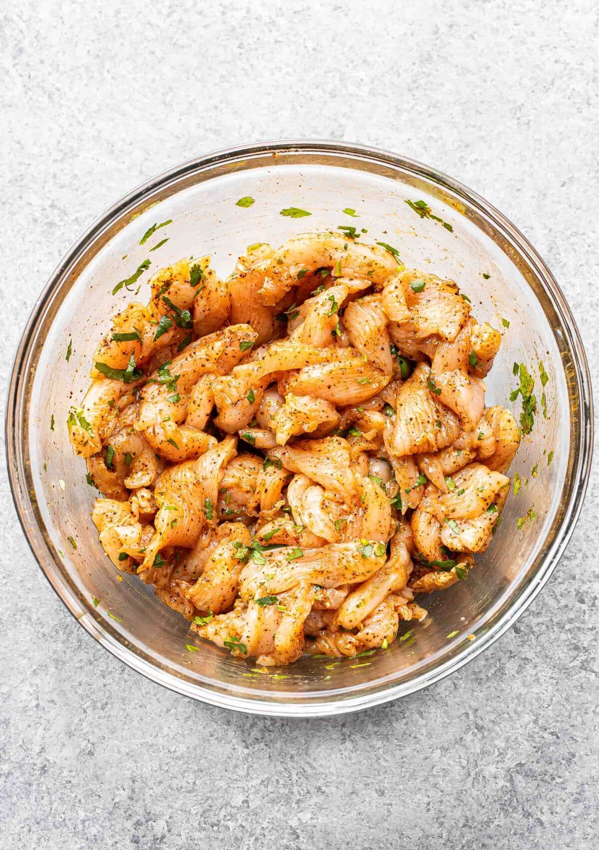 Sliced and marinated chicken for fajitas in a glass bowl.
