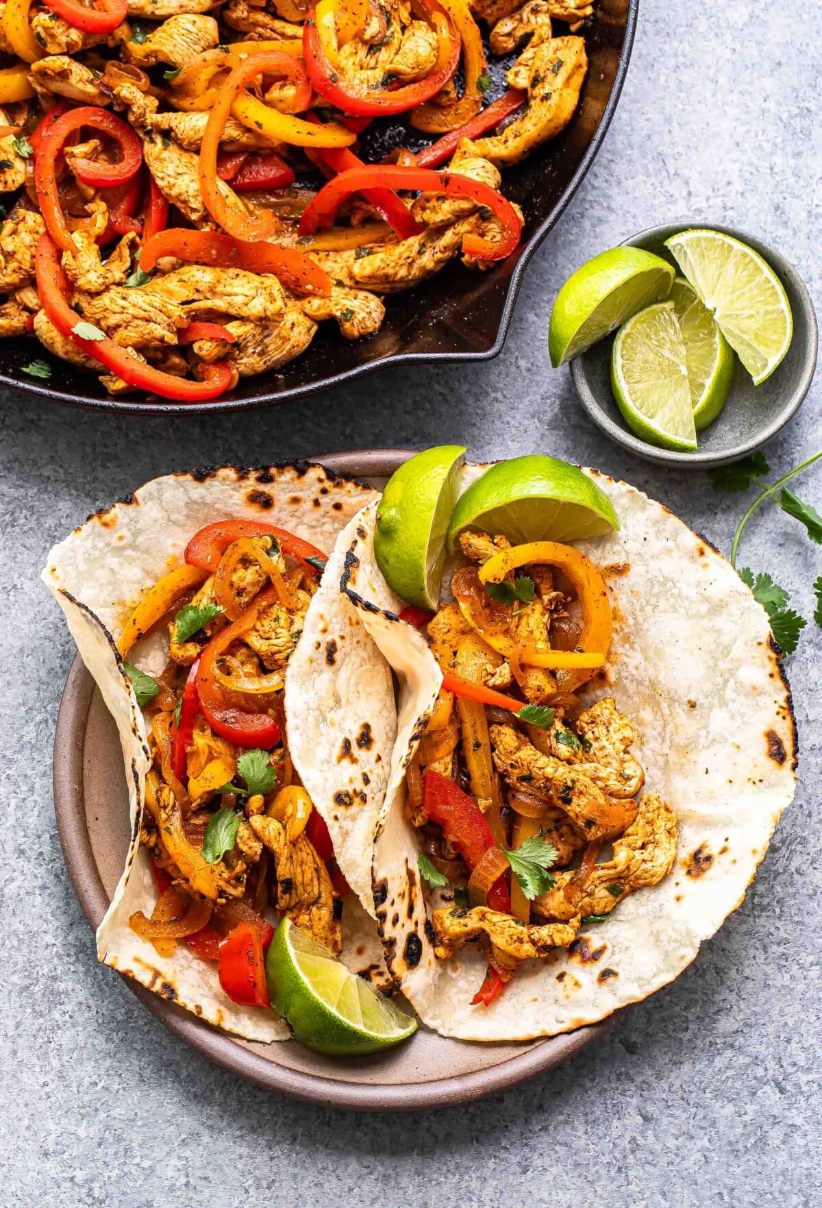 Two chicken fajitas in flour tortillas with lime wedges next to them.