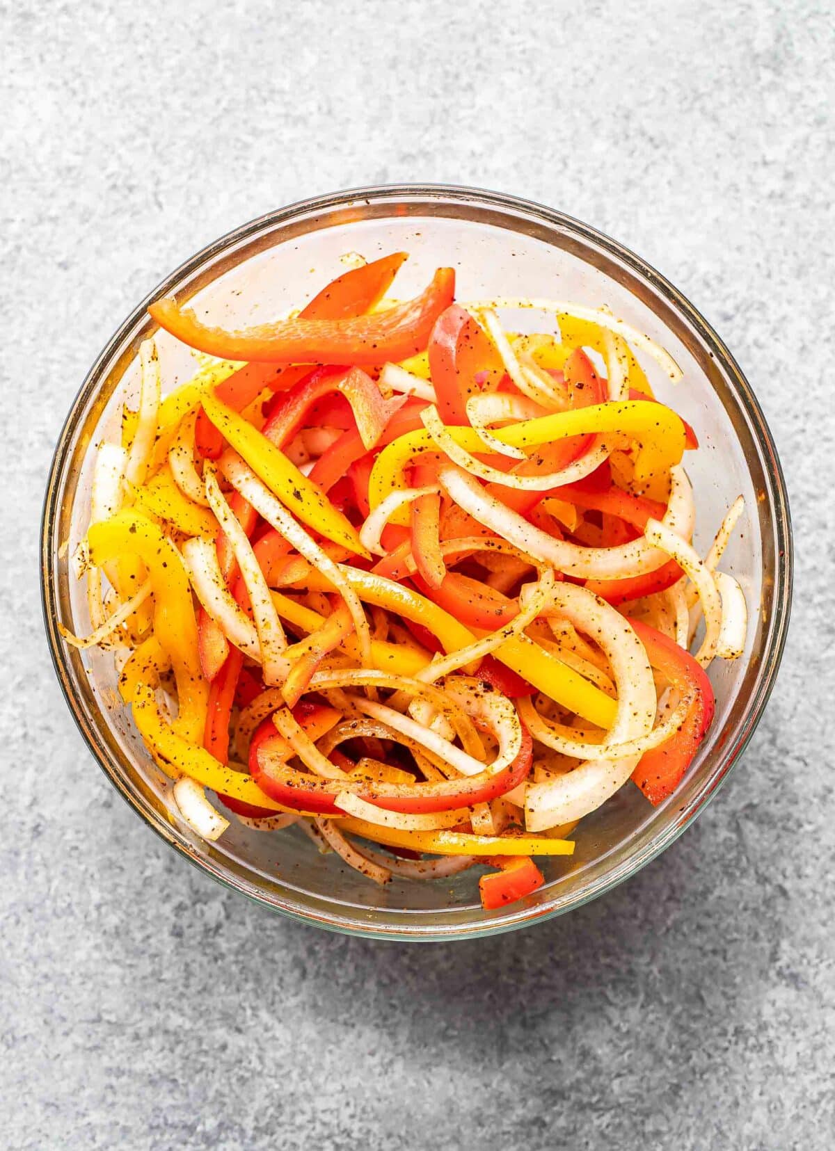 Sliced peppers and onions in a glass bowl.