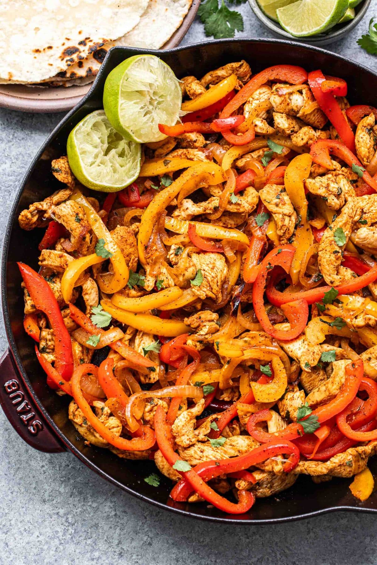 Chicken Fajitas in a skillet with two lime halves.