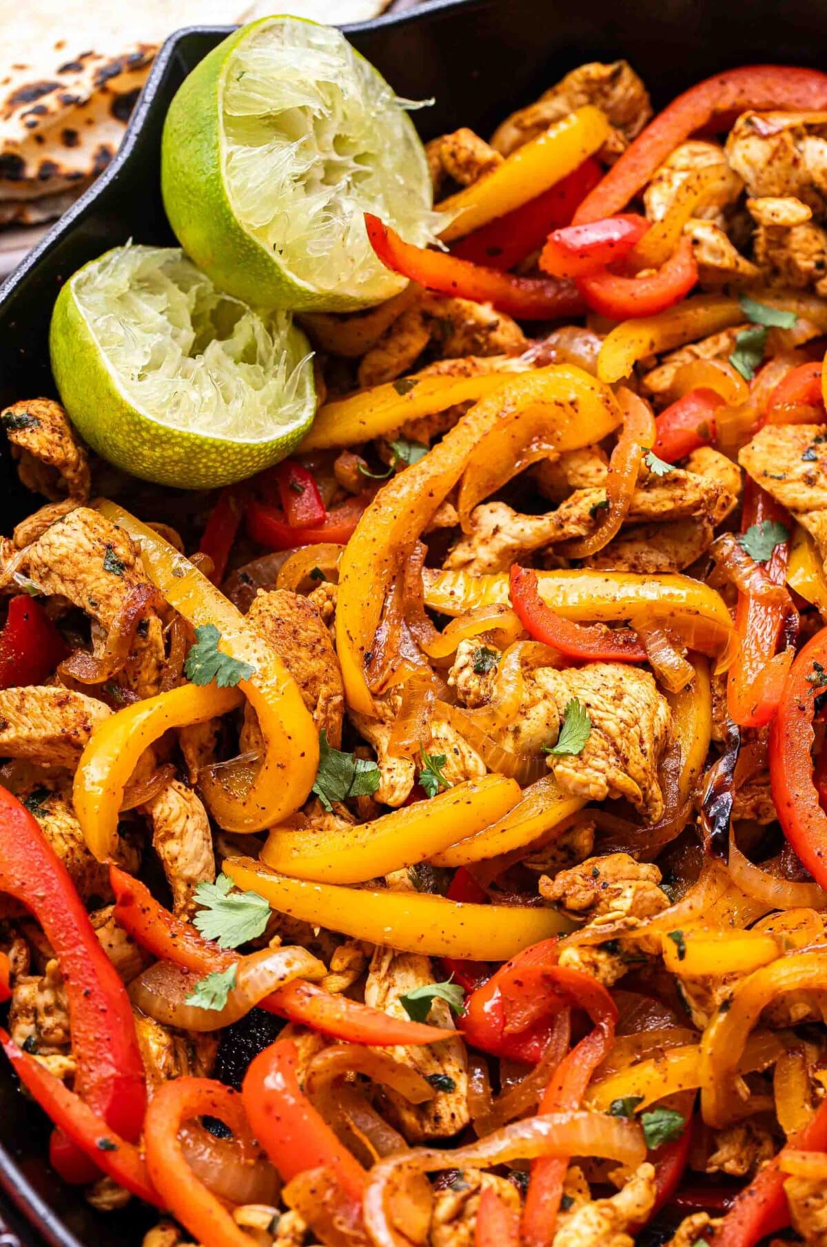 Chicken Fajitas in a skillet with two lime halves.