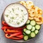 Whipped Feta Dip in a bowl on a serving plate with crackers, cucumbers, and peppers.