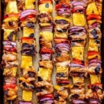 Overhead photo of six Hawaiian chicken, pineapple, red bell pepper and red onion chicken skewers on a sheet pan.