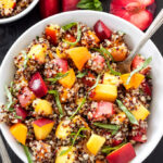 Stone Fruit Quinoa Salad in white serving bowl with spoon. Plums and apricot on the side.
