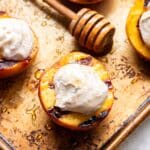 Grilled peach topped with ricotta and a honey spoon behind it.