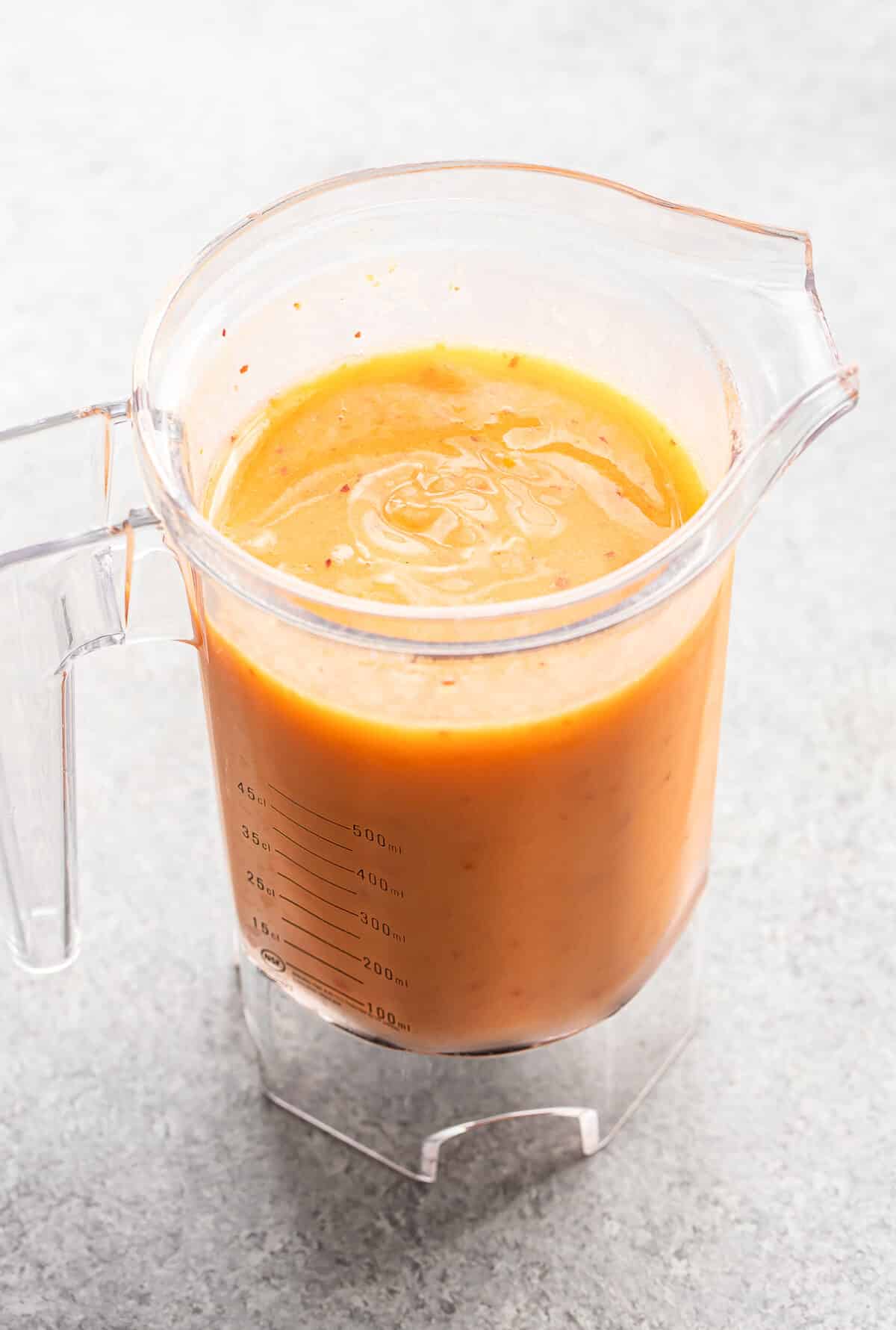 A clear blender pitcher filled with creamy orange soup sits on a gray countertop, reminiscent of the vibrant hues found in a Bourbon Peach Slush.