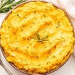 White serving bowl with Mashed Butternut Squash with Goat Cheese and Rosemary in it and a serving spoon next to the bowl.