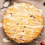 Overhead photo of Cranberry Orange Yogurt Cake on parchment paper with cranberries scattered around it and a jar of the glaze behind it.