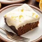 A slice of gingerbread cake with lemon cream cheese frosting on a white plate with a fork.