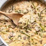 Wooden spoon in a skillet of creamy chicken, asparagus, and mushrooms.