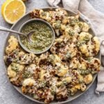 Parmesan Pesto Roasted Cauliflower on a plate with a bowl of pesto and a halved lemon behind the plate.
