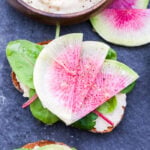 White Bean Crostini with Watermelon Radishes on slate serving stone and a small wooden bowl filled with the white bean purée