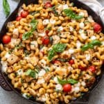 Caprese chicken pasta in a skillet toppeed with mozzarella cheese and basil.