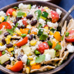 Southwest Vegetarian Pasta Salad with tomatoes, black beans, corn in a wooden bowl with spoon.