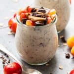 Jar of cherry overnight oats topped with chopped cherries and chocolate. A spoon and cherries are next to the jar.