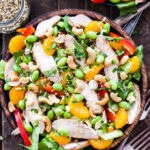 Asian Sesame Chicken and Cashew Salad in a bowl with forks next to it and a bowl of cashews and vinaigrette behind it.