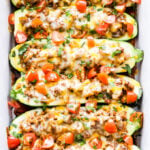Overhead photo of six Taco Stuffed Zucchini Boats filled with ground beef and topped with melted cheese, tomatoes and cilantro.