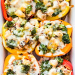 six Cheesy Broccoli, Chicken and Rice Stuffed Peppers in a white casserole dish