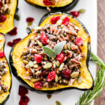 half of an acorn squash on a white plate stuffed with a mixture of wild rice, lentil, herbs and dried cranberries.