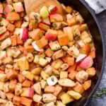 Maple mustard chicken and sweet potatoes in a cast iron skillet with a wooden spoon in the skillet.