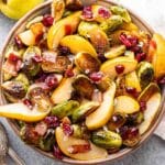 Roasted Brussels Sprouts with Bacon and Pears and dried cranberries in a serving bowl with pears behind the bowl.