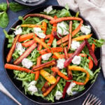 Five-Spice Roasted Carrot Salad with Mint Tahini Yogurt Sauce drizzled on top on a black plate. Blue background with a small bowl of the yogurt sauce next to the plate.