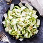 Zucchini Ribbon Salad with Lemon and Parmesan Cheese in black bowl with a small bowl of pine nuts on the side.