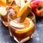 Apple Cider Old Fashioned in a glass garnished with an orange and apple slice and a cinnamon stick.